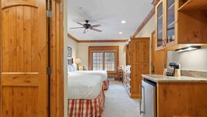 A bedroom with two beds, a wooden wardrobe, and a kitchenette with a refrigerator. - The Charter at Beaver Creek D255 (Beaver Creek)