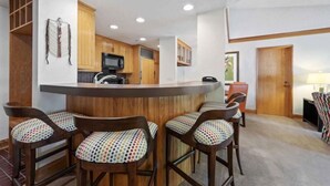 A kitchen with wooden cabinets, a central island with stools, and a microwave.
