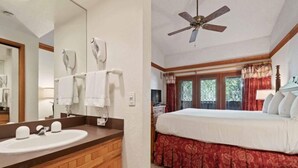 A bathroom with a wooden vanity, a large mirror, and a ceiling fan. The room has a bed with a red bed skirt and a window with curtains.