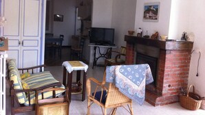 Un soggiorno con divano, poltrone, televisore, camino e zona pranzo sullo sfondo.