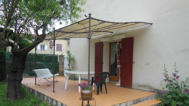 Patio esterno con tavolo e sedie, zona coperta e pianta in vaso.