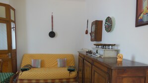 Un soggiorno con un divano giallo, cuscini decorati, un mobiletto in legno e una sveglia a muro.