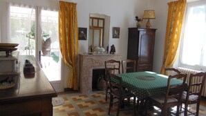 Una sala da pranzo con camino, sedie di legno, un tavolo con tovaglia verde e tende gialle.