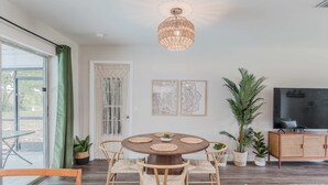 A dining area with a round table, four chairs, a chandelier, and a television on a cabinet.