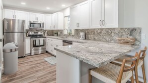 A modern kitchen with white cabinets, stainless steel appliances, a granite countertop, and a small island with wicker chairs.