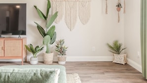 A living room with a television, a rattan cabinet, and several potted plants.