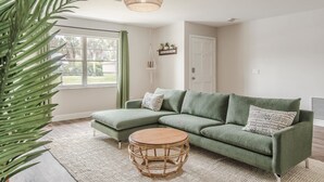 A green sectional sofa with patterned pillows, a round wooden coffee table, and a large potted plant.
