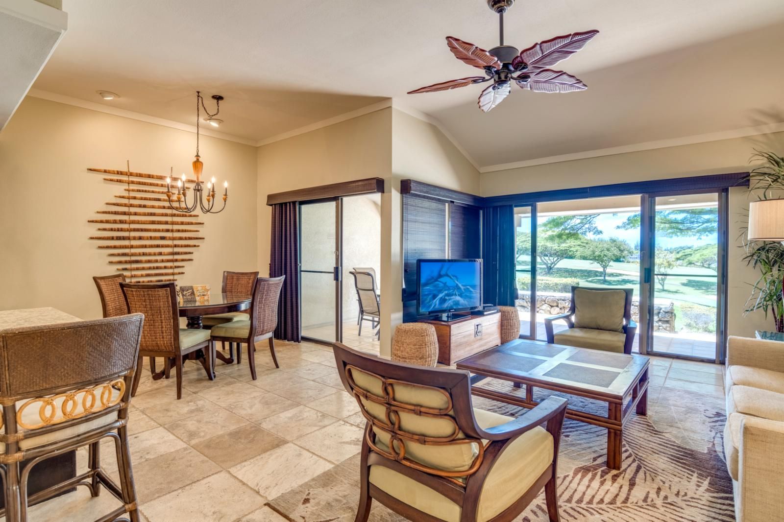 A spacious living area with a dining table, chairs, a television, and a ceiling fan.