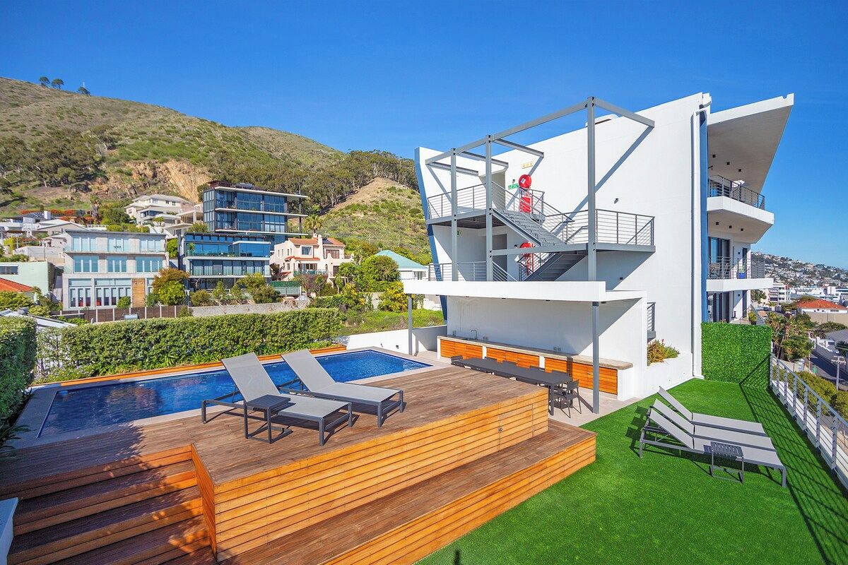 A modern building with a pool, outdoor seating, and a view of the surrounding area.