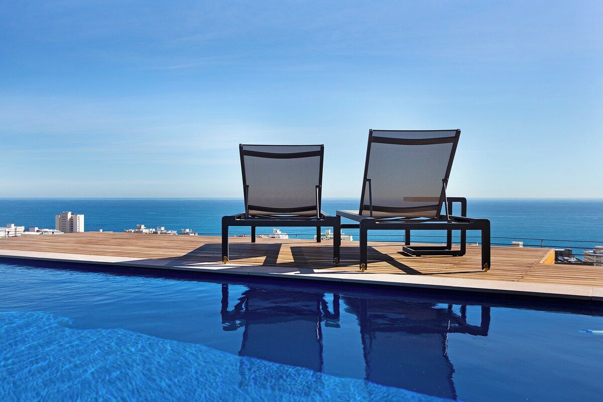 A poolside area with two chairs facing the ocean, a wooden deck, and a clear view of the sea.