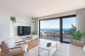 Una sala de estar moderna con un televisor de pantalla plana, un sofá, una mesa de centro y un balcón con vista al mar.