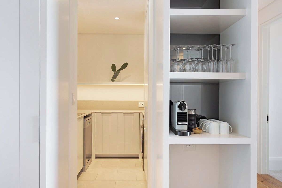 A modern kitchen with white cabinetry, a built-in dishwasher, and a coffee machine on the countertop.