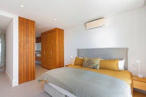 Un dormitorio con cama, mesitas de noche, un equipo de aire acondicionado y un armario de madera.