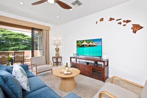 A modern living room with a sofa, chairs, a coffee table, and a TV displaying a tropical scene.