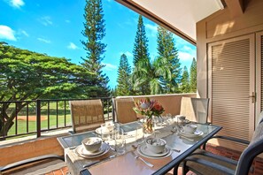 A dining table set for four on a balcony with a view of a golf course and tall trees.