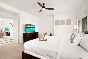 Une chambre d’hôtel équipée d’un lit, d’une télévision, d’un ventilateur de plafond et donnant sur la chambre voisine.