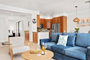 A modern living room with a blue sofa, wooden coffee table, and a dining area with wooden cabinets and a kitchen island.