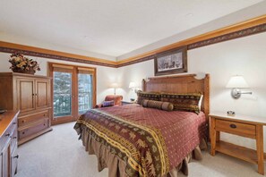A bedroom with a large bed, wooden headboard, two bedside lamps, a nightstand, a dresser, and a window with a view of trees. - "Inviting 2BR Condo at The Charter C350 – Centrally Located with Classic Appeal (Beaver Creek)