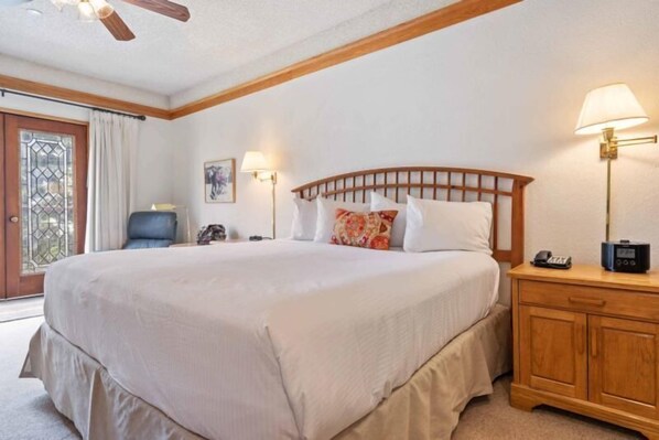 A large bed with a wooden headboard, a bedside table with a lamp, and a nightstand with a phone. - The Charter at Beaver Creek C335 (Beaver Creek)