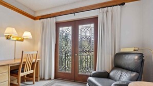 Ein Zimmer mit einem Holztisch, zwei Stühlen, einem Ledersofa, einem kleinen Tisch und einem großen Fenster mit Vorhängen.