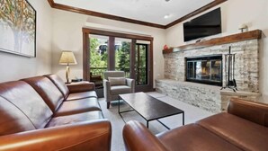 A modern living room with leather sofas, a stone fireplace, and a large TV mounted above it. - The Charter at Beaver Creek C230 (Beaver Creek)
