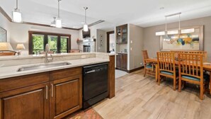 A modern kitchen with wooden cabinets, a dishwasher, and a dining area with wooden chairs and a table. - The Charter at Beaver Creek C230 (Beaver Creek)