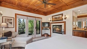 Un dormitorio amplio con una cama grande, chimenea, ventilador de techo y vistas al exterior a través de un ventanal corredero.