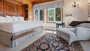 Un dormitorio con una cama grande, una silla, una mesita y una ventana con vistas a árboles.