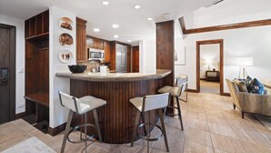 Una cocina moderna con una isla central, taburetes de bar, armarios de madera y un microondas.