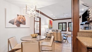 Amplia sala de estar con una mesa de comedor redonda, asientos cómodos, una gran obra de arte de un oso y una pared de piedra con un estante decorativo.