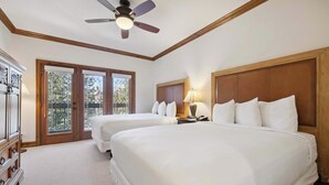 A hotel room with two beds, a ceiling fan, a wooden headboard, a nightstand with a lamp, and a view through a glass door. - The Charter at Beaver Creek C125 (Beaver Creek)