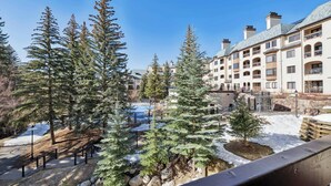 A resort with a snow-covered landscape, tall evergreen trees, and a building with multiple balconies. - The Charter at Beaver Creek C125 (Beaver Creek)
