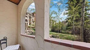 A balcony with a white chair and a view of a garden and buildings.