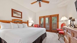 A bedroom with a large bed, a ceiling fan, a wooden dresser, and a red chair.