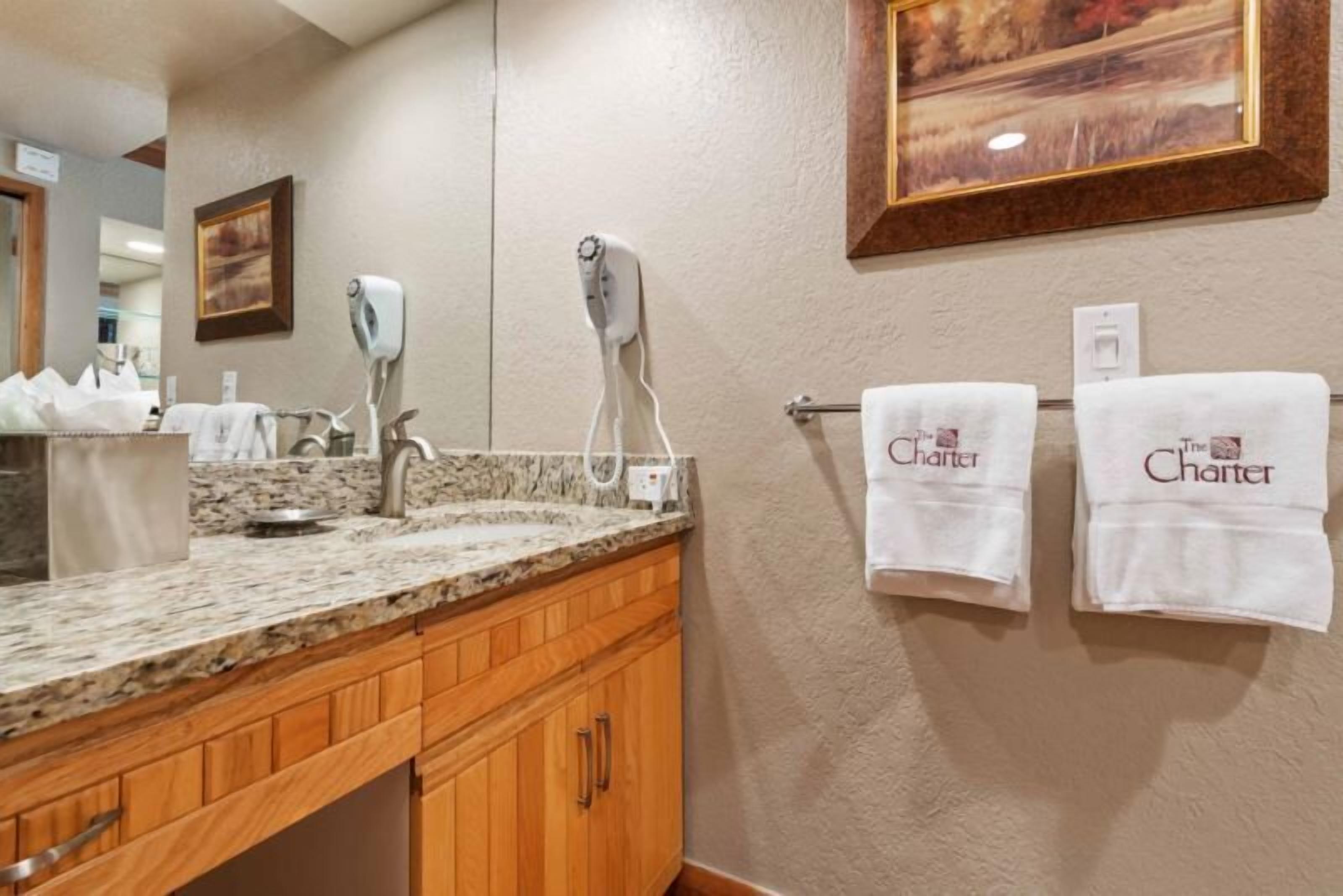 A bathroom with a granite countertop, wooden cabinets, a hairdryer, and two towels hanging on a towel rack.