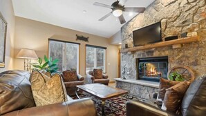 A cozy living room with leather sofas, a stone fireplace, a flat-screen TV, and a ceiling fan. - The Charter at Beaver Creek B430 (Beaver Creek)