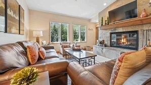 A living room with a fireplace, leather sofas, a coffee table, and a TV mounted above the fireplace.