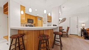 Une cuisine avec des meubles en bois, un plan de travail blanc et trois tabourets.