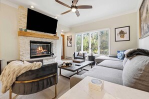 A living room with a fireplace, a ceiling fan, a large window, and a sofa.