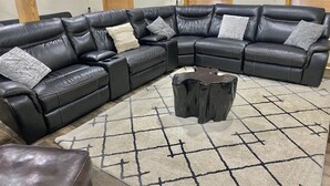 Un canapé d’angle en cuir noir, doté de plusieurs coussins, une table basse noire et un tapis à motifs dans un salon.