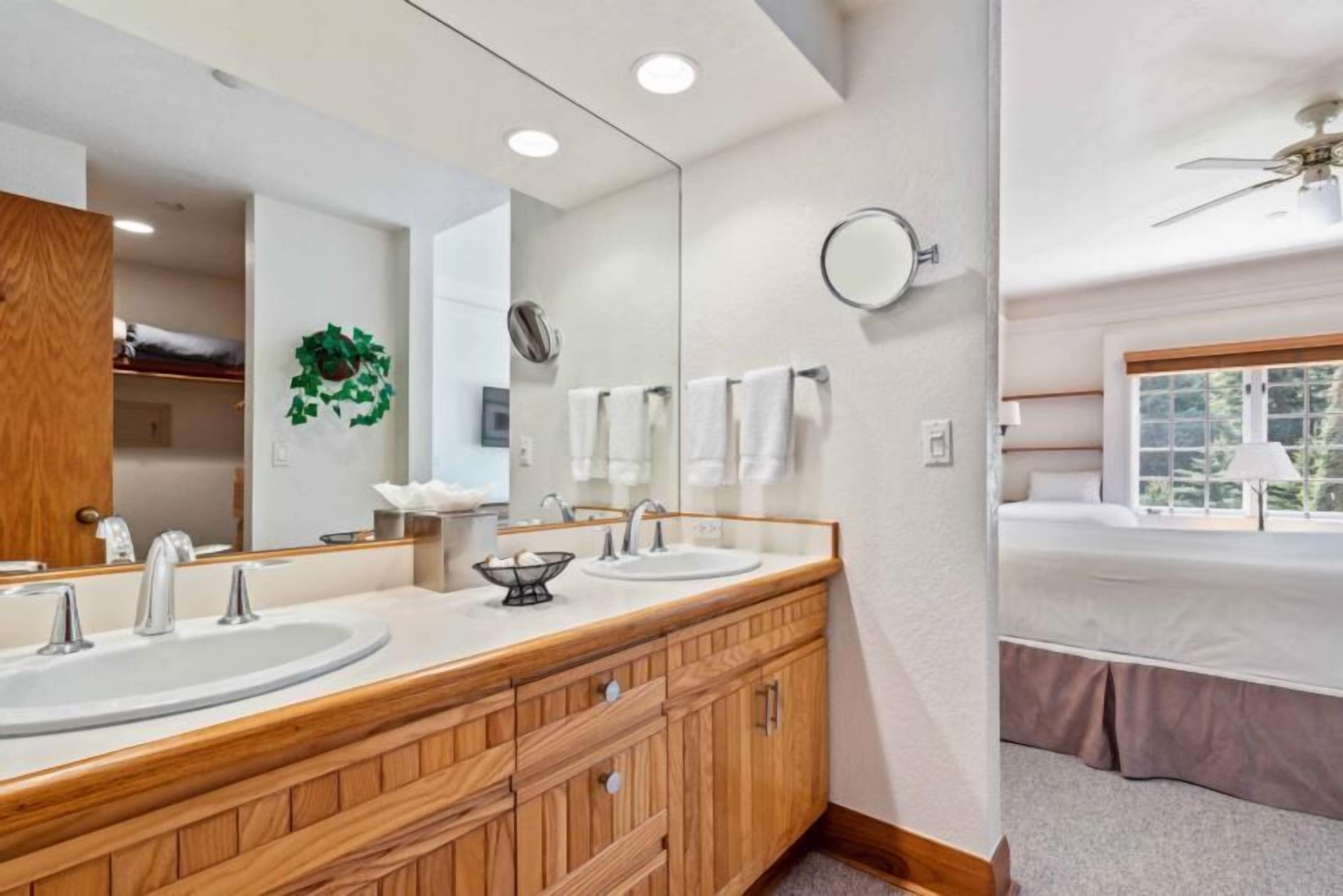 Une salle de bain moderne avec deux lavabos, un grand miroir et une fenêtre donnant sur un paysage verdoyant.