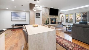 Una sala de estar moderna con chimenea, un televisor grande montado en la pared y una zona de estar con sofá y sillones.