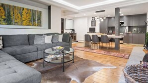 Una sala de estar moderna con un sofá gris, una mesa de centro de vidrio y un comedor con una mesa y sillas blancas.