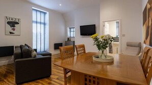 A modern living room with a wooden dining table, a sofa, and a TV mounted on the wall. - Inviting 1-bed Apartment in Lytham Saint Annes (Lytham St. Anne's)