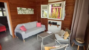 Una habitación acogedora con techo de madera, ventilador de techo, sofá, una mesita y una silla de mimbre.