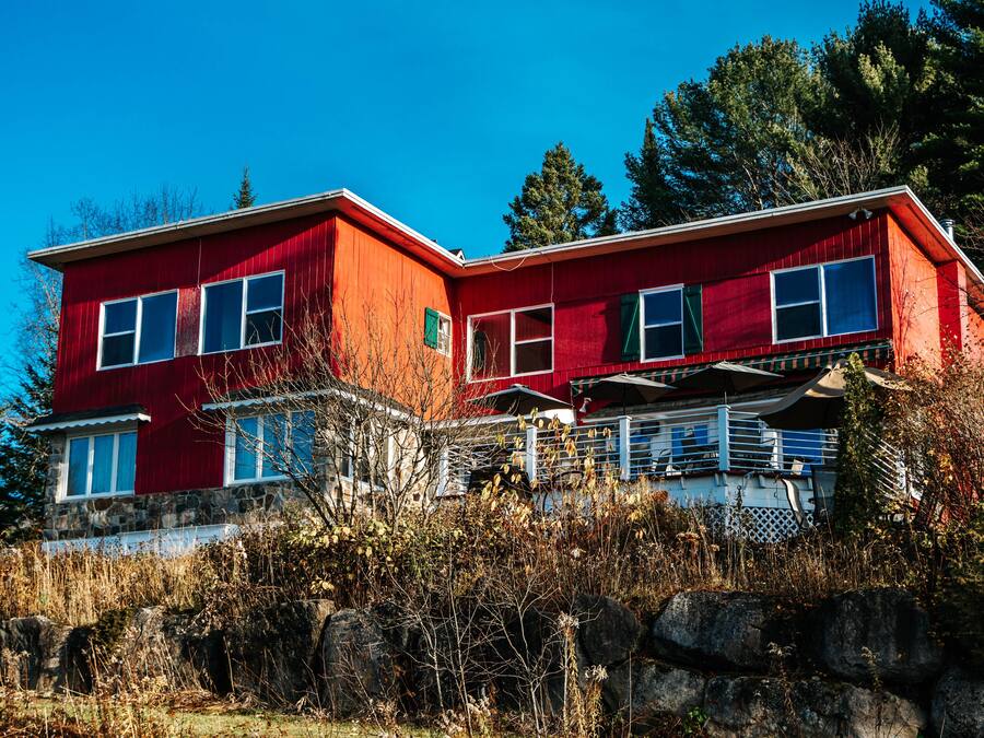 A red two-story house with a stone foundation, large windows, and a balcony.