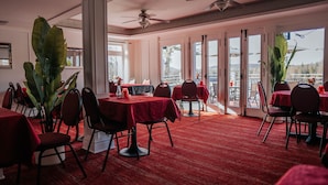 A dining area with tables covered in red tablecloths, chairs, and large potted plants. - Auberge Lac du Pin Rouge (Saint-Hippolyte)