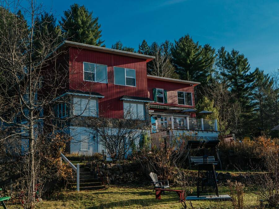 A two-story red house with a balcony, surrounded by trees and a grassy yard.