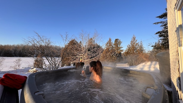 A hot tub with a person inside, surrounded by a snowy landscape and trees. - Auberge Lac du Pin Rouge (Saint-Hippolyte)
