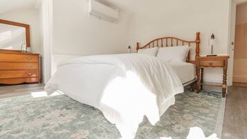 Una cama bien hecha con cabecera de madera, una mesita de noche con lámpara y un aparador con cajones.
